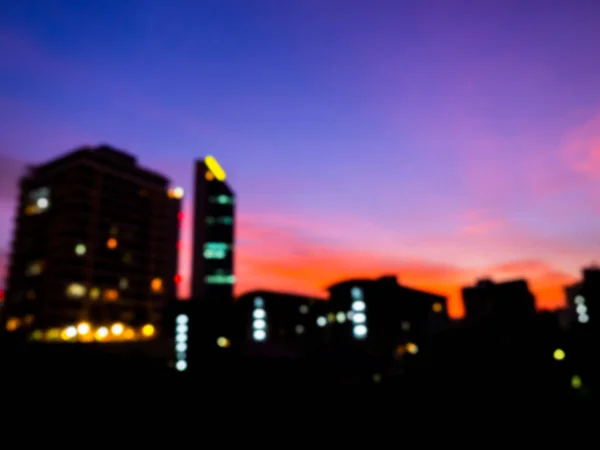 建物のぼやけたシルエット 紫と青の空の背景の街並み 日没後に暗い上のビジネスビルでカラフルなライトをブリュリー 概要夜の都市背景 — ストック写真