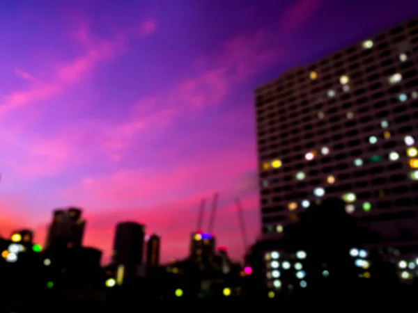 Blurred silhouette of building, cityscape on purple and blue sky background. Blurry colorful lights with business building on dark after sunset. Abstract night urban backgrounds.