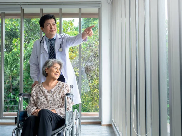 Uśmiechnięta Azjatka Seniorka Siedzi Wózku Inwalidzkim Podczas Gdy Lekarz Białym — Zdjęcie stockowe