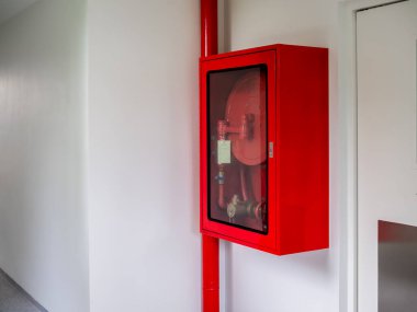 Fire extinguisher cabinet mounted on the wall in the corner of the white hotel building. Locked red emergency box with fire extinguisher and fire hose reel, safety equipment for prevent fire.
