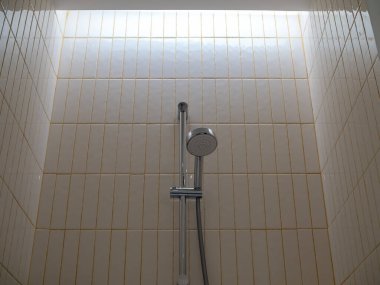 Paslanmaz çelik duş ve demirler eski fayansların duvarına monte edilmiş. Modern otel banyosundaki sarı harç desenli dikey desen..