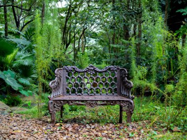 Empty old lonely vintage iron bench seat, chair at the desolate yard on the green forest background.