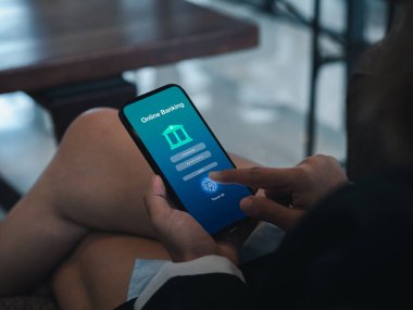 Mobile banking concept. Online banking application page on smart mobile phone screen holding by businessperson hand scanning with fingerprint for login. Electronic banking transaction technology.