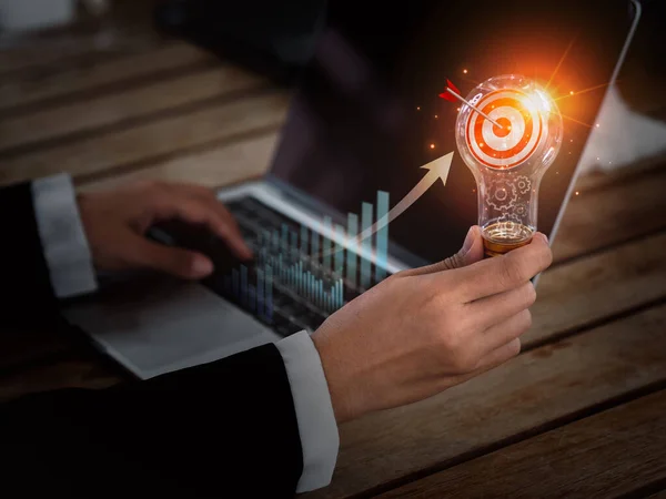 Digital marketing business success concept. Target 3d icon in creative idea light bulb holding by business person hand who working with laptop computer. Creative motivation for successful business.