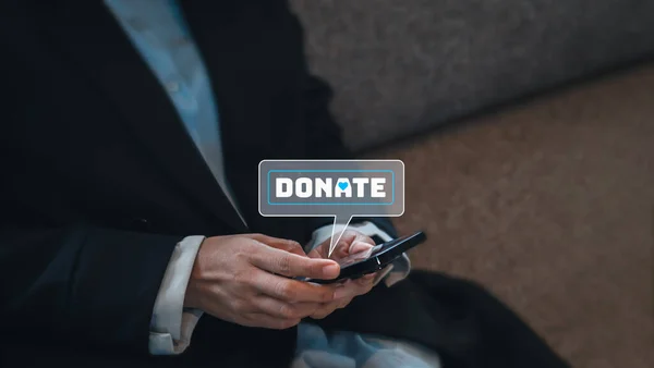 Close-up donate icon in bubble speech symbol appear on smart mobile phone in businessperson\'s hands in suit, sit on couch with copy space. Donation online by cellphone concept.