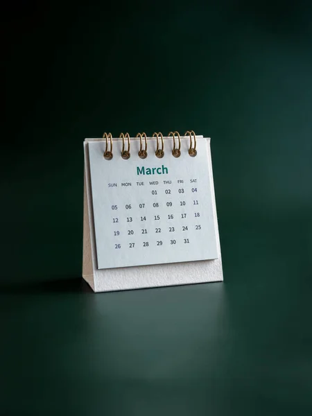 A March 2023 calendar desk for the organizer to plan and reminder isolated on dark green background, vertical, minimal style. White small table calendar with the page of the third month.