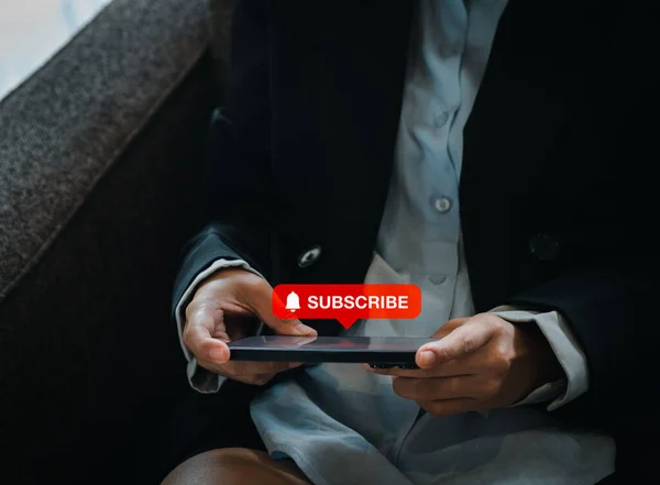 Subscription concept. Big red subscribe button with bell icon appear on smart mobile phone in hand. Smartphone horizontal style holding by businesswoman who watching on entertainment applicatiion.