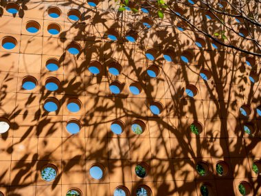 Terracotta ventilation circular brick block wall with circle space pattern wall background with tree shade. Concrete cement air outdoor decoration.