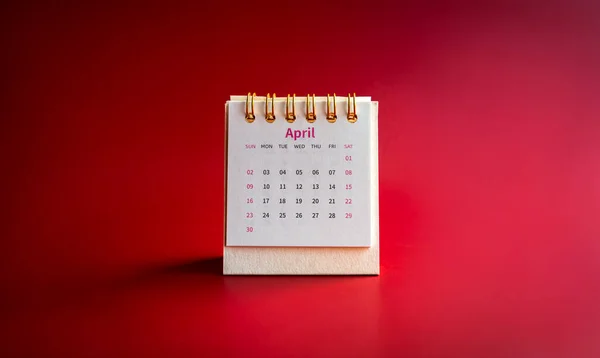 April 2023 calendar desk for the organizer to plan and reminder isolated on red background, minimal style. Small white table calendar with the page of the fourth month, front view.