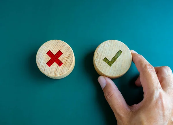 Right and wrong. Close-up green check mark and red X mark icon on round wooden button, chosen green check mark by business\'s hand. Picking correct sign. Approving, voting or right decision concepts.