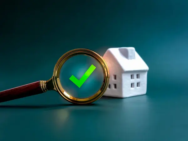 stock image House online search, property survey, buying, selling and real estate finding concepts. Digital green checkmark glowing on gold magnifying glass with small white house on blue background.