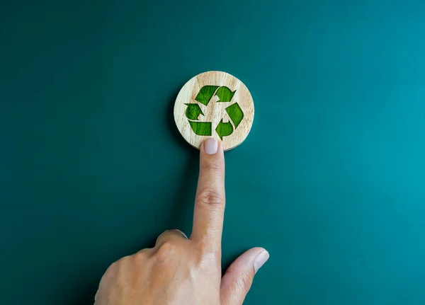 Green recycle icon symbol on round wooden block, pointing by hand isolated on blue background. Ecology, sustainability cooperation, reduce, reuse and recycle concepts. Campaign for green recycling.