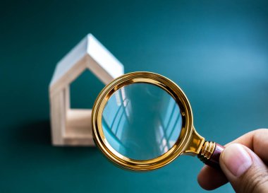 House online search, property survey, buying, selling and real estate finding concepts. Empty blank space for text or logo on lens of gold magnifying glass with white wood house on blue background.