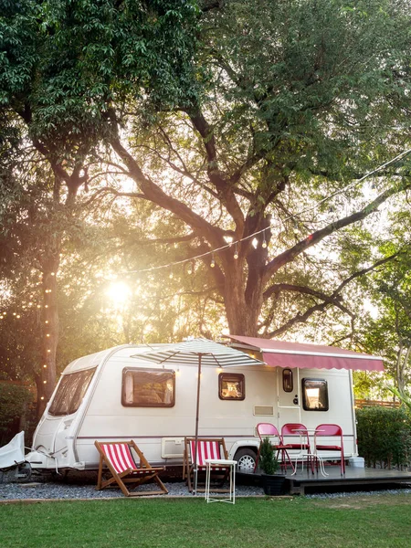 Vintage caravan car parking in garden decoration with empty seats and table on big tree background, vertical style. Relax camping and sleep in the motorhome trailer. Family vacation travel concept.