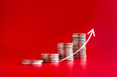 Grafik çizelgesi kırmızı zemin üzerinde izole edilirken bozuk para yığınları üzerinde yükselen ok. Yatırım, tasarruf, mali gelir, satın alma eğilimi artışı, enflasyon, iş pazarlama büyüme kavramları.