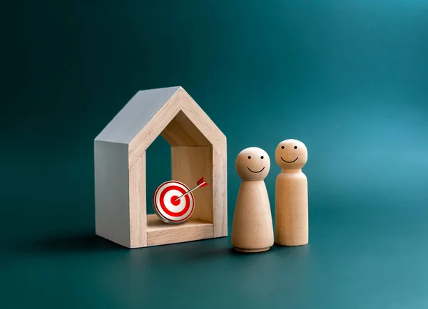 Family planning, building family, real estate investment concept. Happy smiling of couple lover wooden figure standing near white wood house model with 3d target icon inside on blue background.