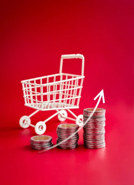 stock image Online shopping sale profit, sales increase, business marketing, inflation concepts. Rising arrow on coin stack as a graph step near white shopping cart trolley on red background, vertical style.