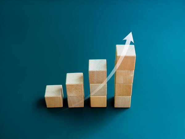 White rising up arrow draw on wooden cube blocks bar graph chart steps on blue background, minimal style. Purchase trend increase, income, inflation, business marketing growth concepts.