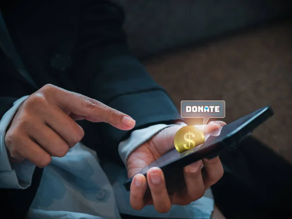 Close-up digital golden coin and donate icon appear on smart mobile phone on donation application or website, pressing by businessperson\'s hands. Donation online by cellphone app concept.