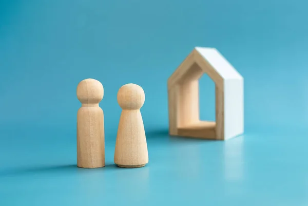 Love couple wooden figure model, male and female symbol, standing front of minimal white wood house on blue background. Building family. First home, buying house, real estate investment concept.