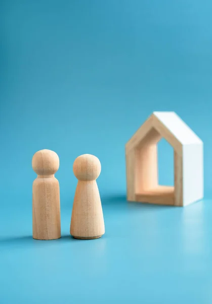 Love couple wooden figure model, male and female symbol, standing front of minimal white wood house on blue background, vertical style. Building family. First home, buying house, real estate concept.