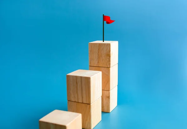 Goal and success. Red flag on the top of wooden cube blocks stacked, bar graph steps. Business growth process, aim, target, development, leadership, marketing, economic improvement concepts.