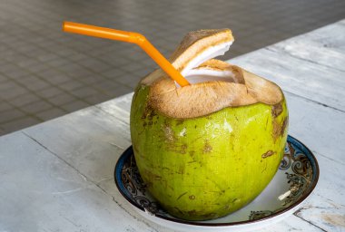 Turuncu renkli taze yeşil hindistan cevizi pipet içiyor. Hindistancevizi tropikal meyvesi en üstte açıldı, içinde taze hindistan cevizi eti ve tatlı su var, yerel bir restoranda servis ediliyor..