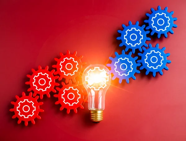 Glowing light bulb connected between blue and red gear wheels on red background. Business strategy, management and solution, human research, connection, teamwork and creative idea concepts.