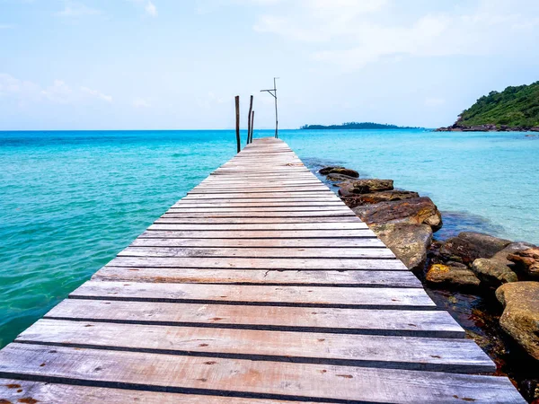 stock image Wooden bridge heading to the blue sea. Brown wood plank pathway bridge on the beach sand with rocks at the local port in the island on sunny day. Seascape summer holiday background.