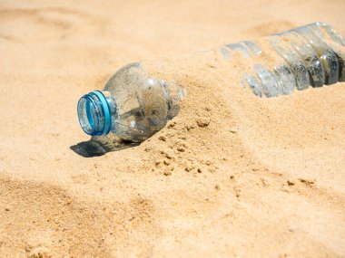 Plastik şişe kumsalda. Kapağı açılmamış boş plastik su şişeleri, kumsala atılmış kumla kaplanmış. Kirli çöpler turistler tarafından terk edildi..