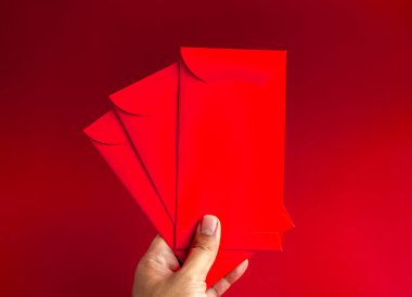 Kırmızı arka planda el ele tutulan üç kırmızı zarf. Çin 'de uğurlu para hediyesi olarak 3 Hongbao paketi, Ocak' ta yeni yıl, kırmızı düğün paketi..