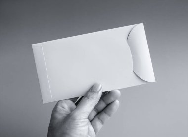 Beyaz bir zarf tutuyor, dikey stil, gri arka planda izole edilmiş, siyah-beyaz tarzda. Yakın çekim boş mektup paketi elinde. İş ve finans kavramı.