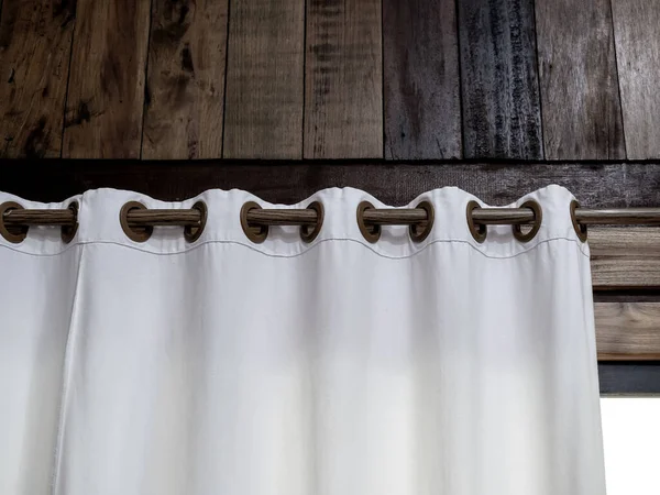 stock image Close-up of white wall curtain on wooden curtain rail bar decorated on the wood plank wall of tropical building over the glass door or window inside room with sunlight from outside.