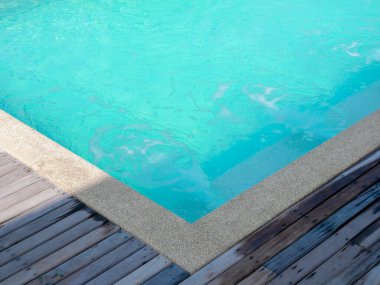 Havuz kenarı zemininin köşesinde açık mavi su havuzu basıncının yanında ahşap tahta güverte var. Güneşli bir günde yüzme havuzunda fotokopi alanı var. Yaz tatili ve seyahat tatili kavramları.