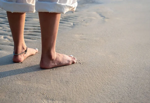 白いパンツを着た裸足の女性が コピースペースのある夕方の夕日の暖かい日差しの中で静かな砂浜に立っています 夏の旅行 レジャー目的地 休暇のコンセプト — ストック写真