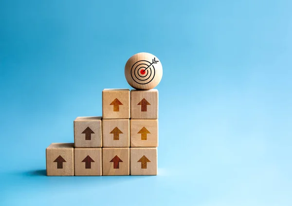 Rise up arrows shoot up towards the goal. Target icon on wooden sphere, top of wood cube block bar graph chart steps on blue background. Business growth process, trend, economic improvement concepts.