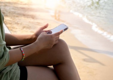 Cep telefonu kullanımı, sosyal medya. Yazın kumsalda arka planda otururken sıradan bir kadının elinde cep telefonuyla siyah boş bir masaüstü görüntüsü.