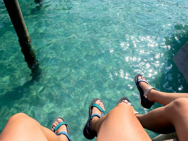 穿着凉鞋的情侣腿 男人和女人坐在海边的桥上 有着复制的空间 夏天阳光明媚的海边放松 假日旅行 — 图库照片