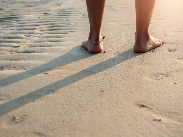 白いパンツを着た裸足の女性の背中側には コピースペースと日没の暖かい日差しの中できれいな砂浜に立っている足が折り畳まれています 夏の旅行 レジャー目的地 休暇のコンセプト — ストック写真