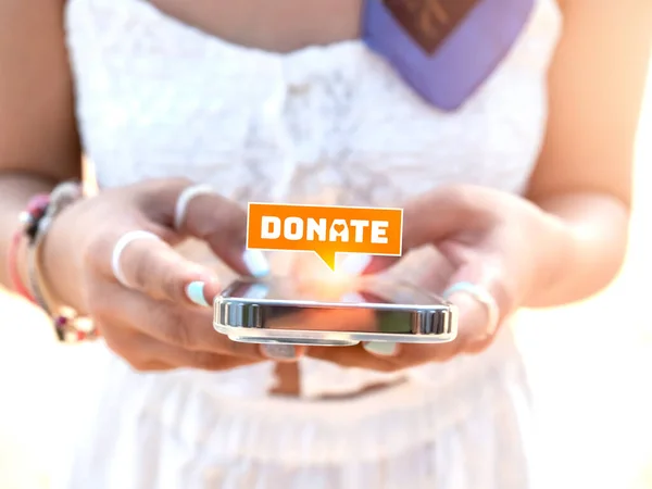 Close-up donate icon in bubble speech symbol appear on smart mobile phone in stylish woman\'s hands in white dress. Donation online on website or application by cell phone concept.