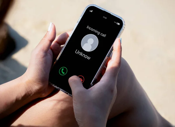 Incoming call with unknown caller, malicious phone calls concept. Unknown number displayed showing on smart mobile phone in woman hand on leave day at the beach. Spam and robocalls, scam call alert.