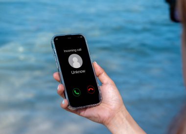 Bilinmeyen arama, kötü niyetli telefon görüşmeleri konsepti. Sahilde izne ayrılan kadının elinde akıllı cep telefonunda bilinmeyen numara görülüyor. Spam ve otomatik aramalar, dolandırıcılık alarmı..