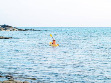 Asyalı kadın can yeleği ve kepli kano kayığıyla denizde kürek çekiyor. Mutlu kadın deniz manzaralı arka planda eğlenceli aktiviteler, tatil gezisi.
