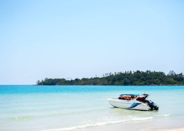 Sahilde kırmızı can yelekli bir seyahat botu mavi denizde beyaz, temiz kumlu bir plaj, yeşil ada ve fotokopi alanı olan açık gökyüzü arka planı. Yaz gezisi konsepti.