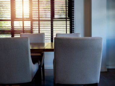 Boş modern gri kumaş sandalyeler, koltuk ve ahşap masa, yemek masası klasik stili, pencerenin yanında sıcak güneş ışığıyla karartılmış. Yemek odası iç dizaynı otel, kapalı mekan..