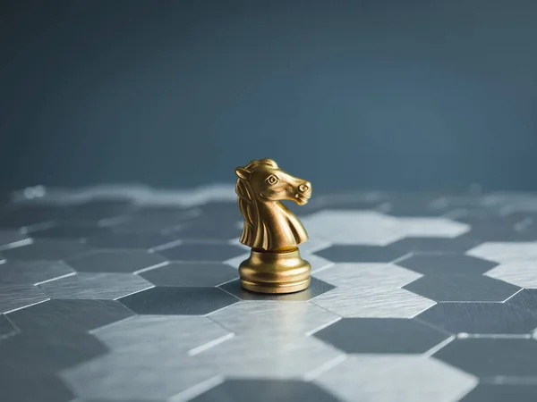The golden horse, knight chess piece standing alone on silver hexagon pattern board and blue background. Leadership, success, team leader, commander, competition, business strategy concept.
