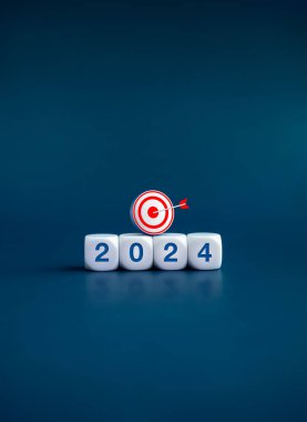 2024 takvim yılı, hedef ve başarı konseptiyle. 2024 ile birlikte beyaz küp bloklardaki 3D hedef simgesi, yeni yıl numarası, koyu mavi afiş arkaplanda izole edilmiş. Mutlu yıllar, iş dikey afişi.