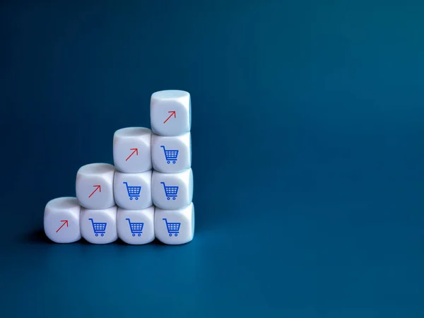 Red rise up arrow and blue shopping cart trolley icons on white cube block stack as a growth graph steps on blue background with copy space. Online shopping and business increase sales profit concept.