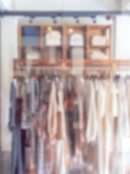 Abstract blurred modern clothes shop interior background, vertical style. Blurry white fashion clothing store with full woman dress hanging rack and wooden shelf with the lights.