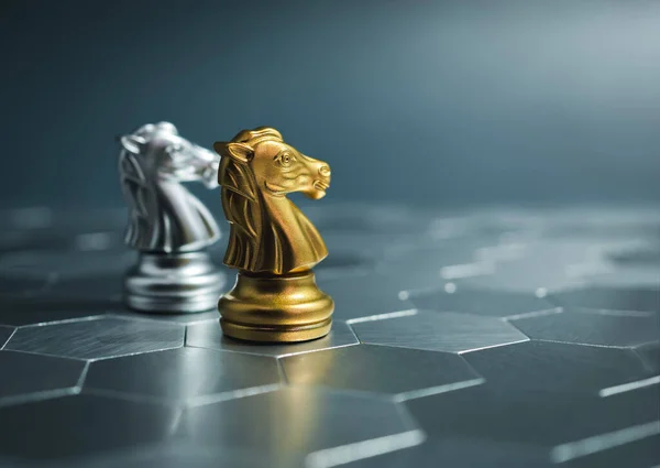 Golden and silver horse, knight chess pieces standing together on a silver hexagon pattern chessboard on blue background. Leader, friend, enemy, cooperation, partnership, business strategy concept.